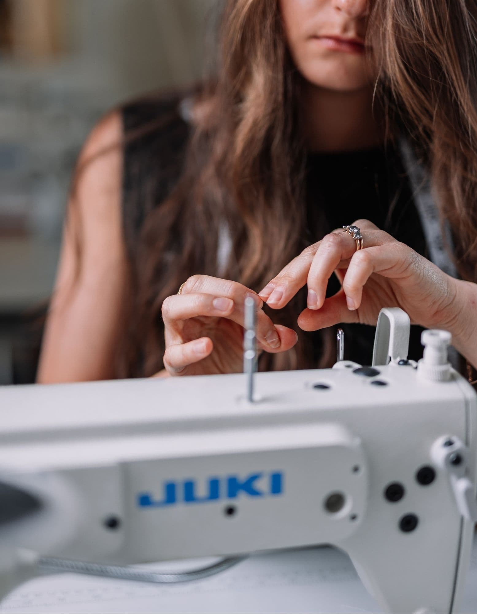 Handwork at the sewing machine Samantha Covey threading a needle beside a Juki sewing machine.
