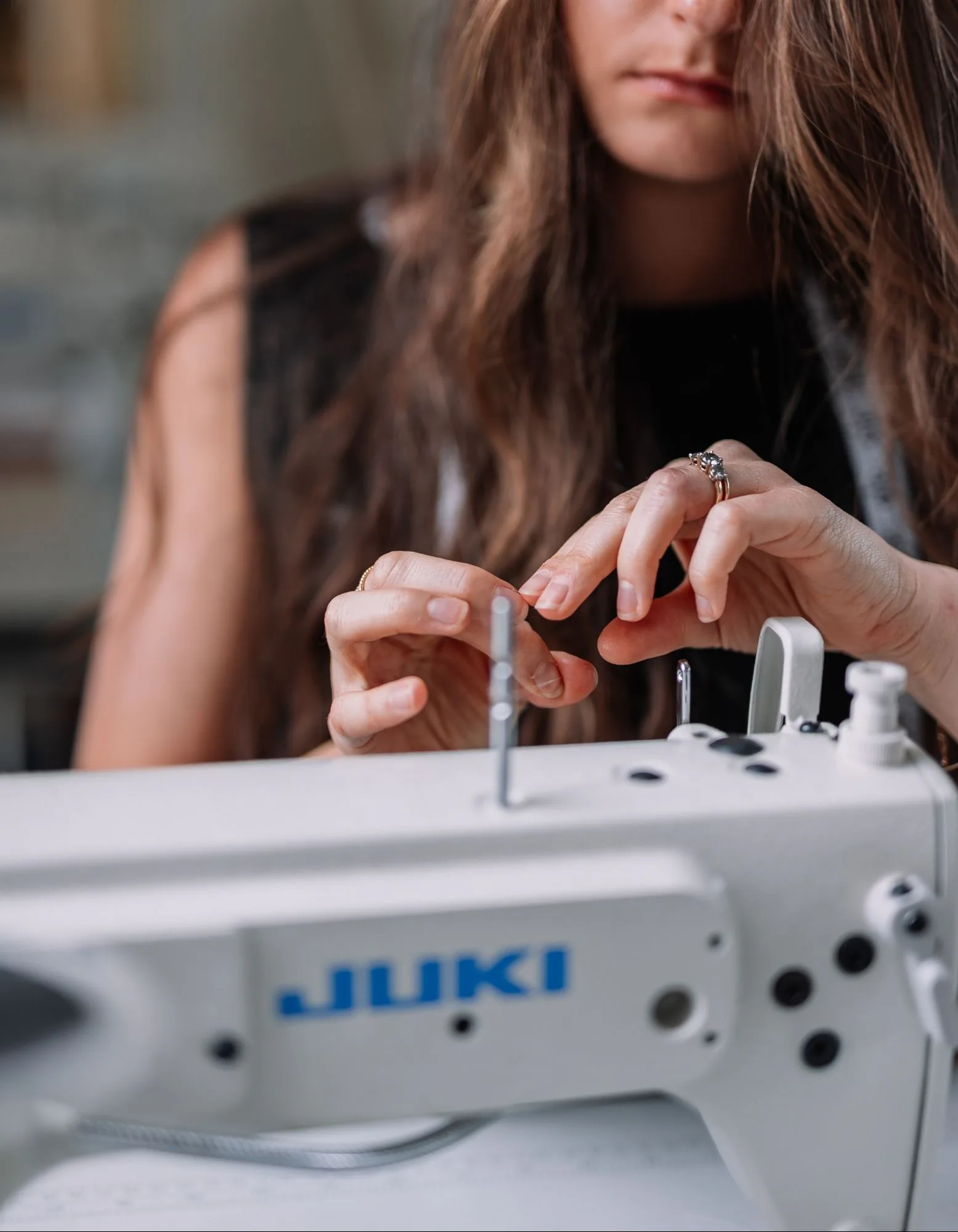 Handwork at the sewing machine Samantha Covey threading a needle beside a Juki sewing machine.